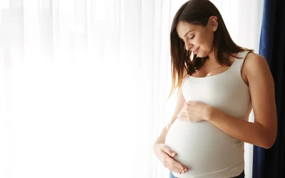 Pregnant woman in a white tank top holding her belly