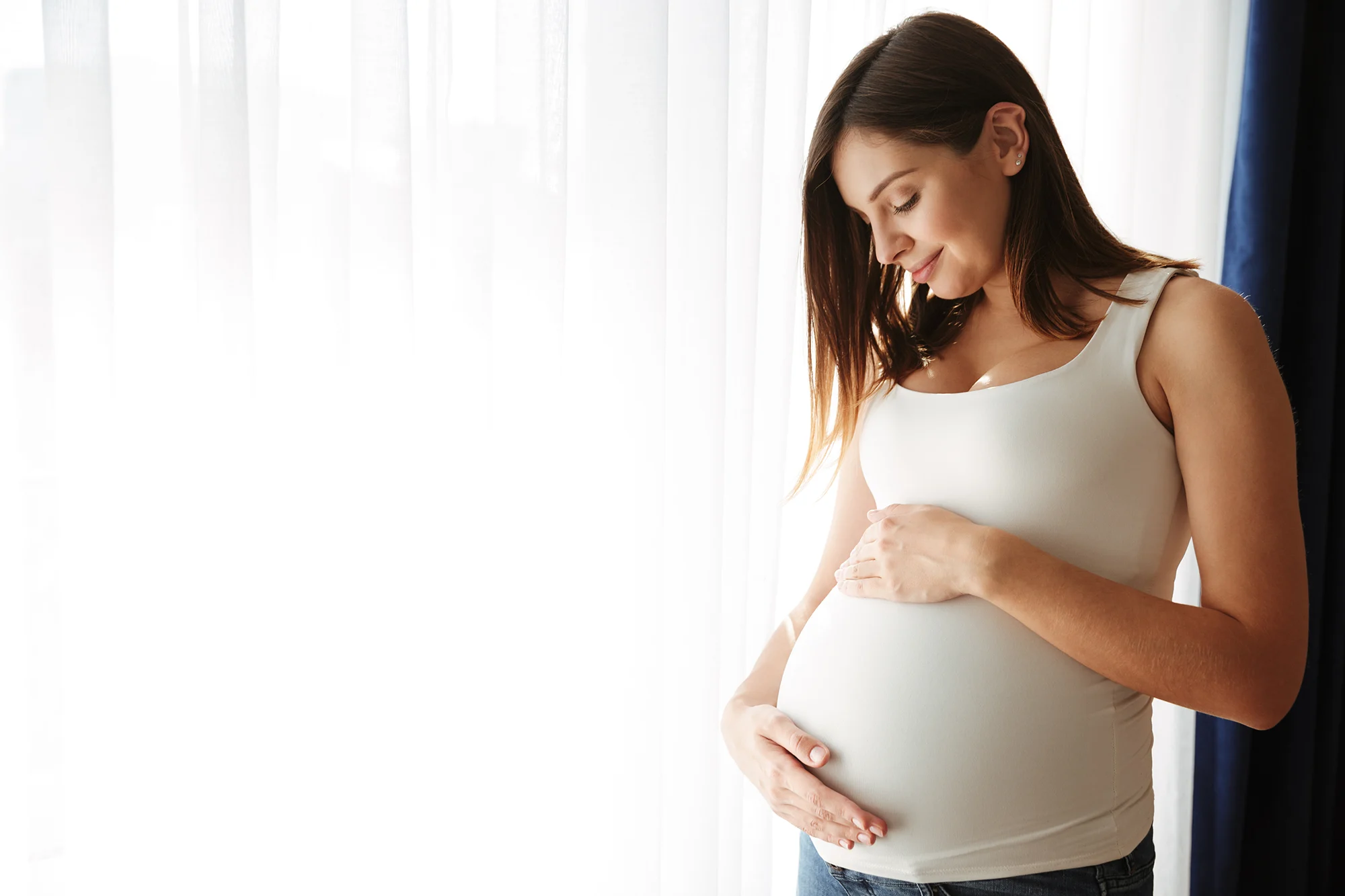 Pregnant woman in a white tank top holding her belly