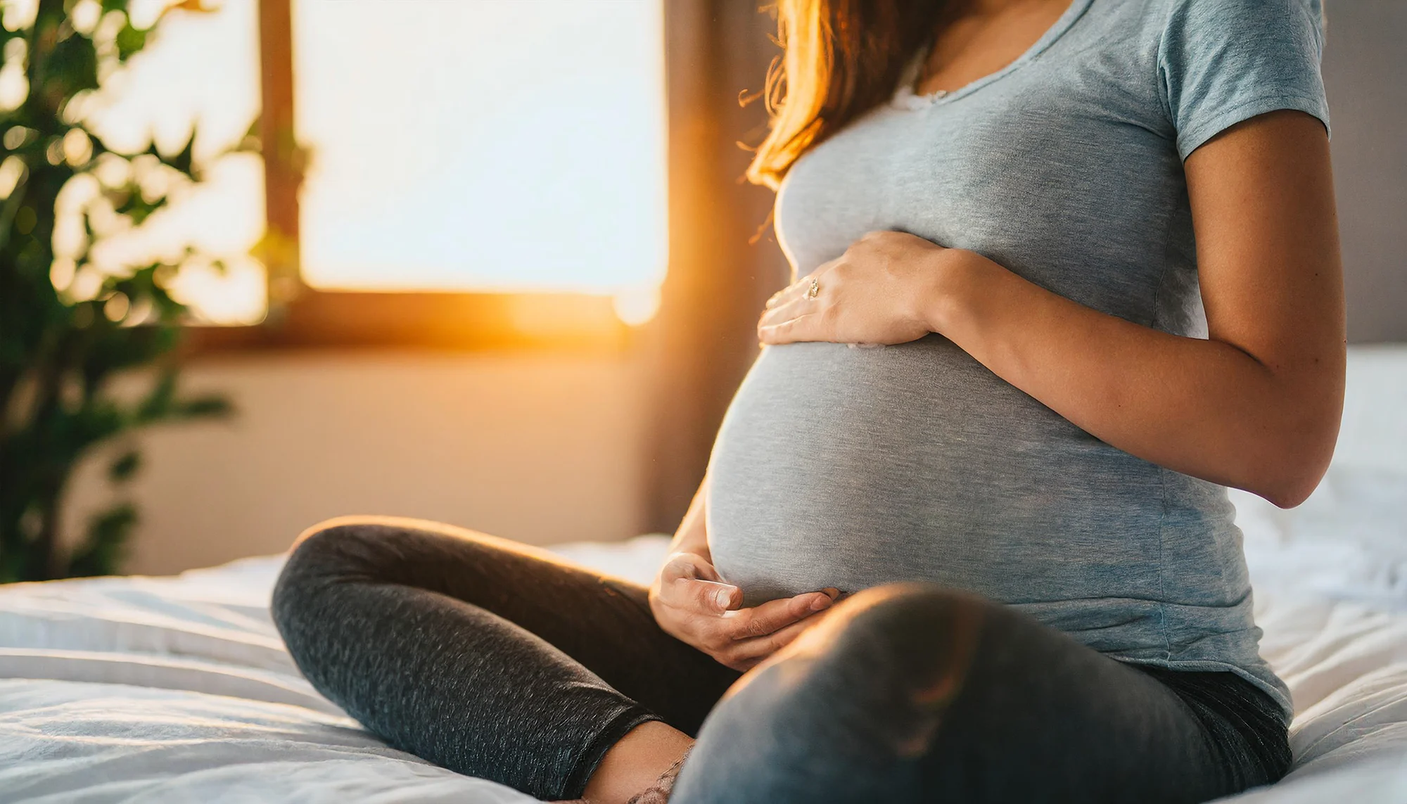 Pregnant woman sitting on a bed with her hands on her belly