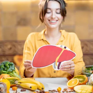 Woman holding a paper liver surrounded by fresh fruit and vegetables Woman holding a paper liver surrounded by fresh fruit and vegetables